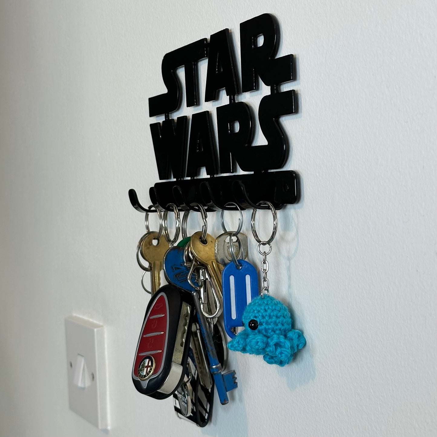 A side view of a black Star Wars logo hanging key rack with 5 small hooks. Hanging from the hooks are two sets of keys, a car key, and two keyrings.