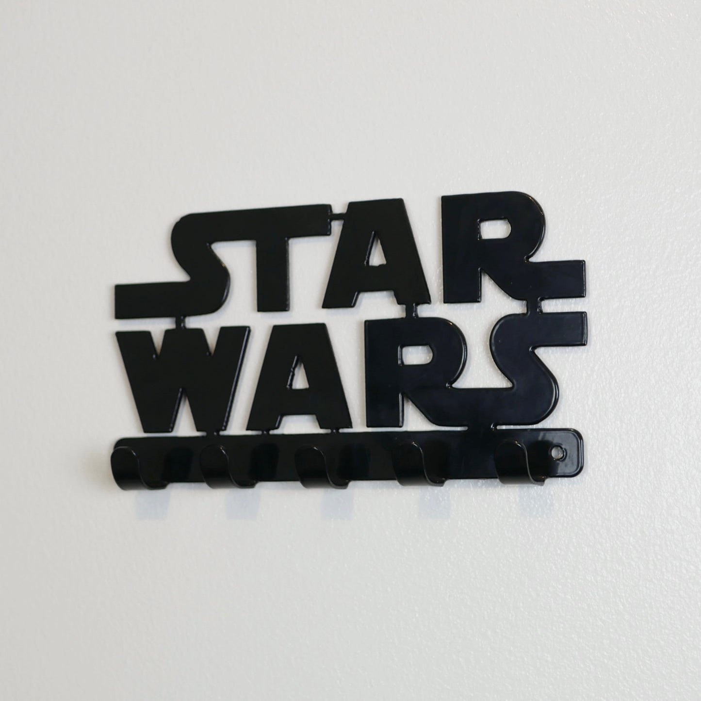 A side view of a black Star Wars logo hanging key rack with five small hooks.