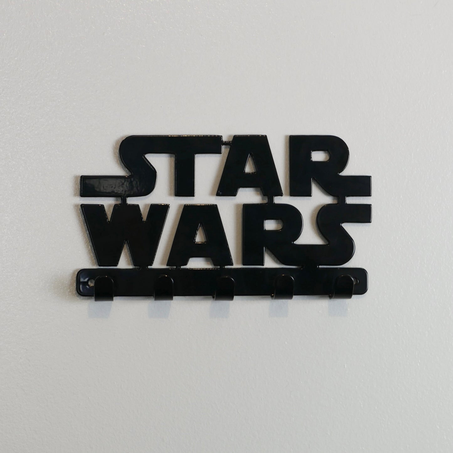 A front view of a black Star Wars logo hanging key rack with five small hooks.