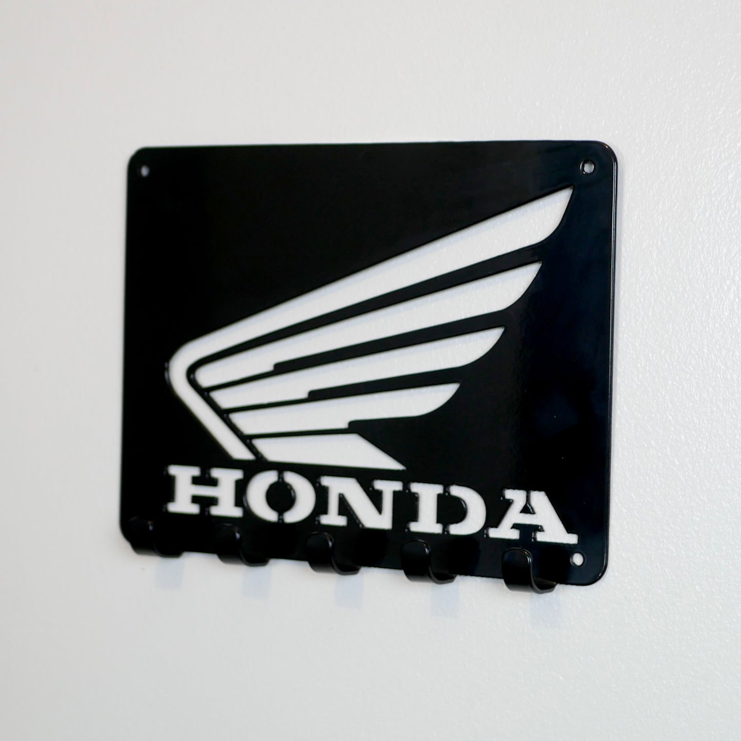 A front view of a black metal Honda logo hanging plaque with five small hooks along the bottom.