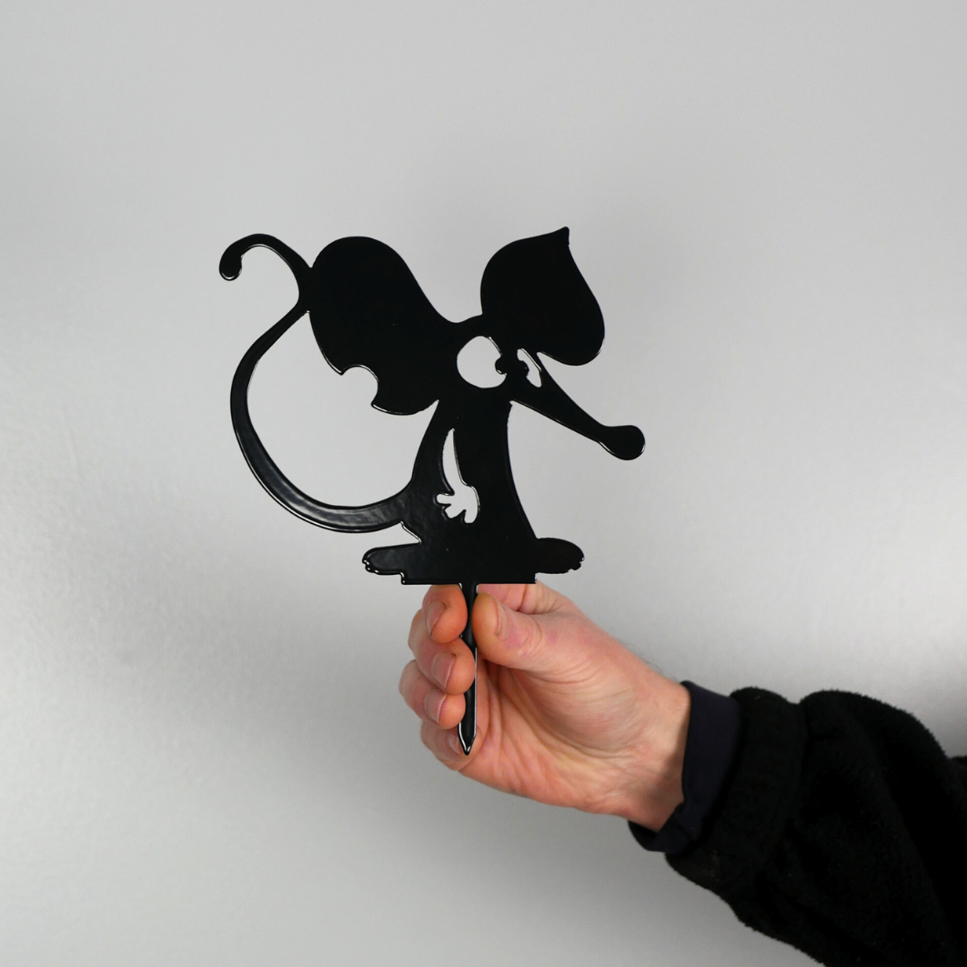 A man’s hand holding a metal black garden stake in the shape of a mouse or a rat.