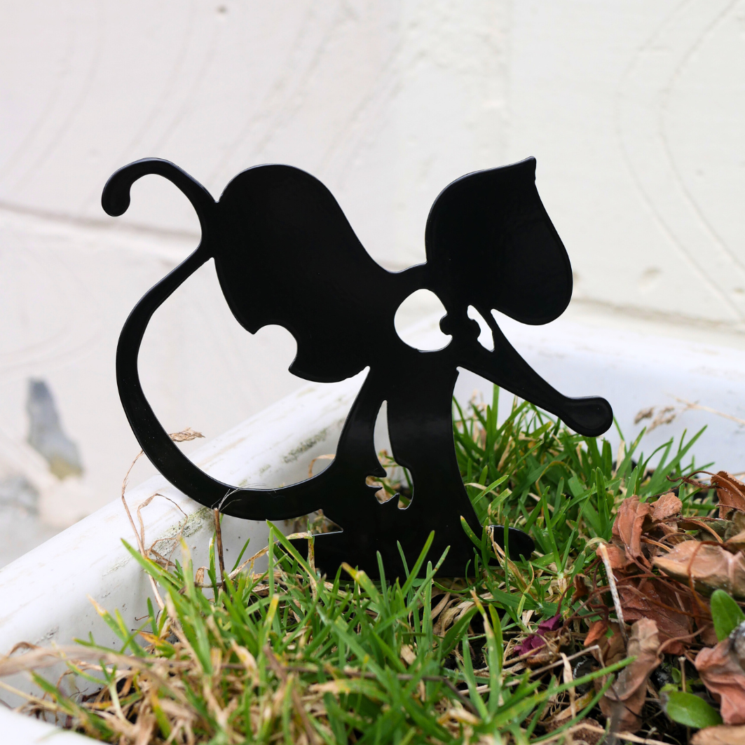 A close up of a metal black garden stake in the shape of a mouse or a rat.