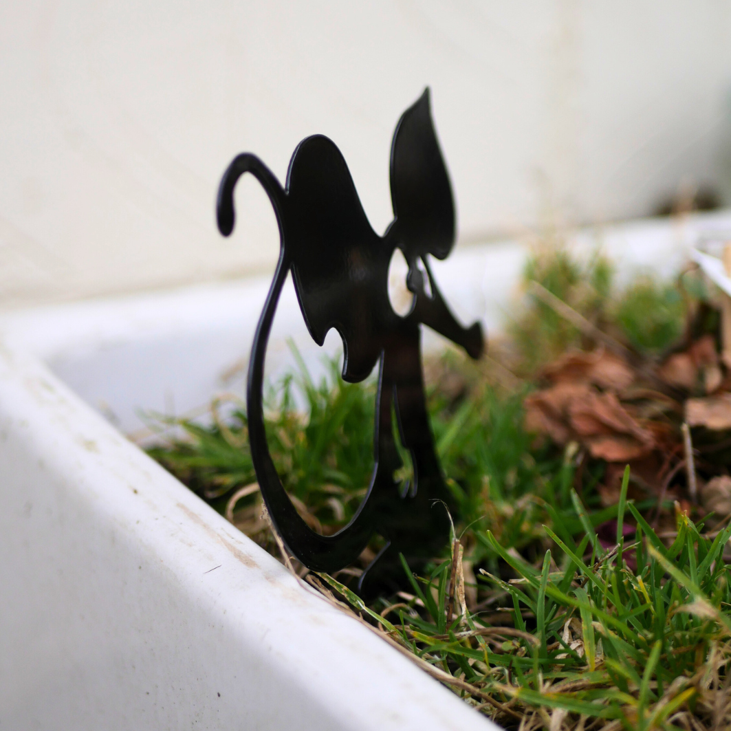 A side view of a metal black garden stake in the shape of a mouse or a rat.
