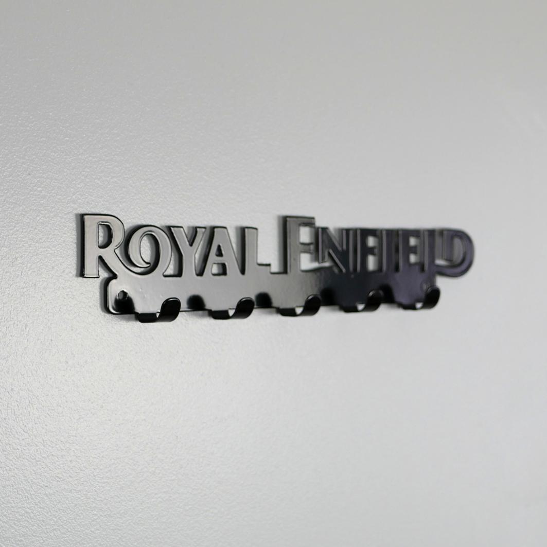 A left side view of a black metal key rack in the shape of the Royal Enfield logo, it has 5 hooks.