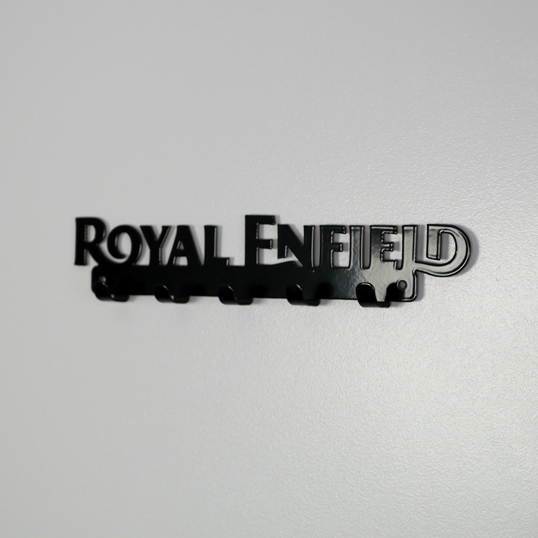 A right side view of a black metal key rack in the shape of the Royal Enfield logo, it has 5 hooks.