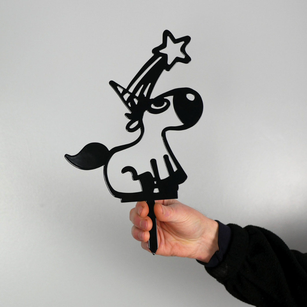 A man’s hand holding a black metal garden stake in the shape of a unicorn. It has a shooting star coming from its horn.