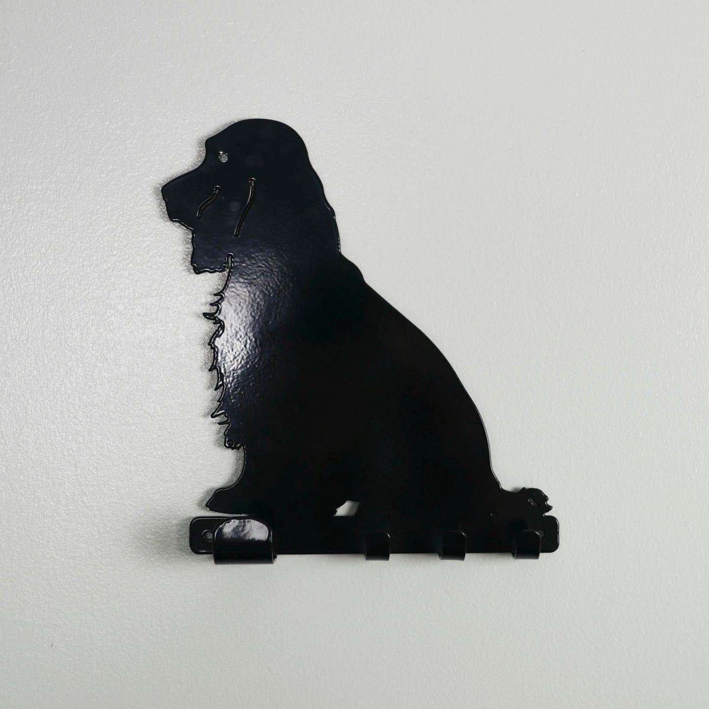 A black cocker spaniel key rack hanging on a white wall. It has one large hook and three smaller hooks along the bottom in a row.