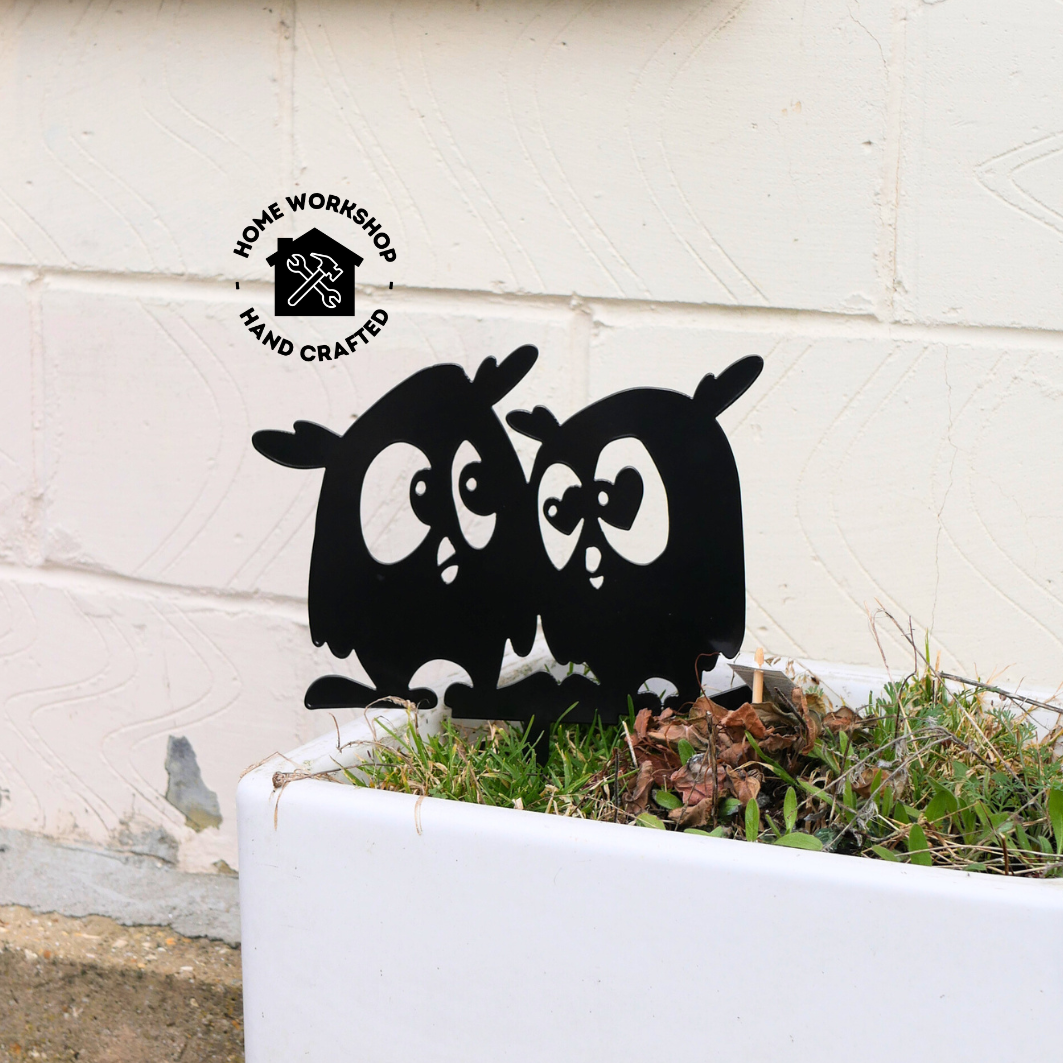 A metal black garden stake in the shape of two owls.