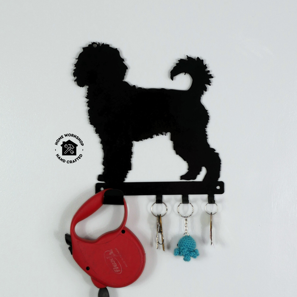 A cockerpoo dog shaped black metal dog lead and key rack, hanging from the four hooks are a dog lead, a keyring, and three keys.