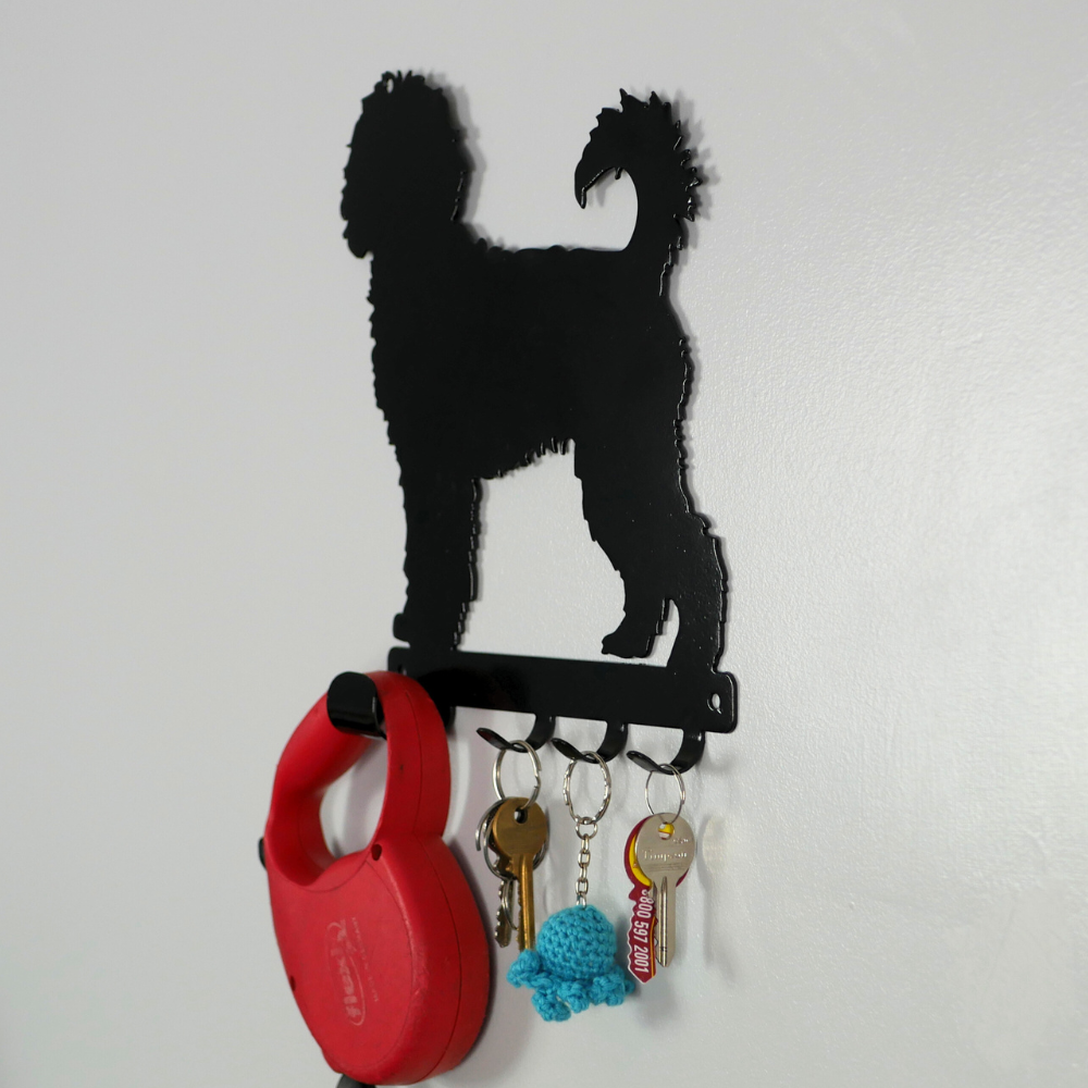 A side angle photo of a cockerpoo dog shaped black metal dog lead and key rack, hanging from the four hooks are a dog lead, a keyring, and three keys.