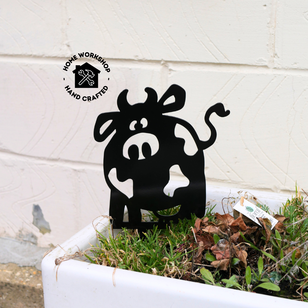 A metal black garden stake in the shape of a cow.