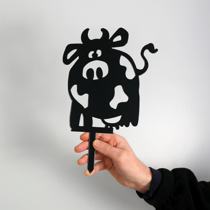 A man’s hand holding a metal black garden stake in the shape of a cow.