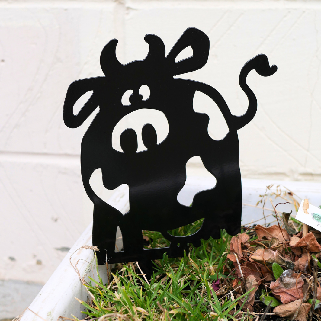 A close up of a metal black garden stake in the shape of a cow.