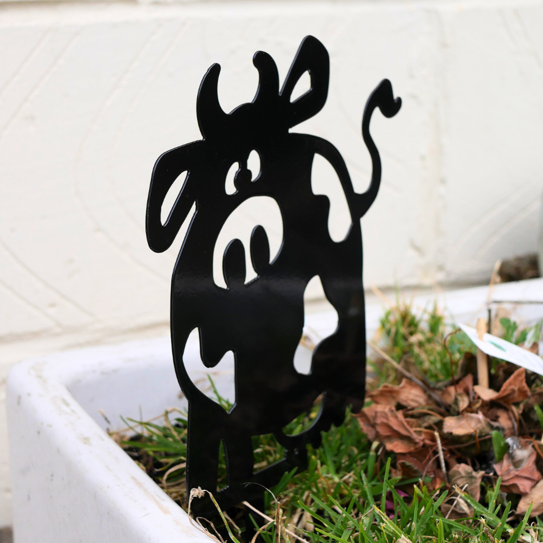 A side view of a metal black garden stake in the shape of a cow.