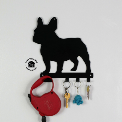 A french bulldog shaped metal black dog lead and key rack. Hanging from the four hooks are a dog lead, keyring, and two keys.