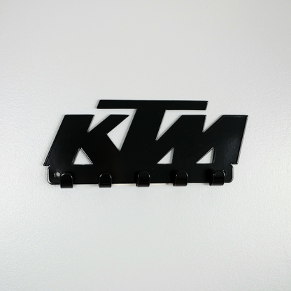 A black metal key rack in the shape of the KTM racing logo, it has 5 hooks.