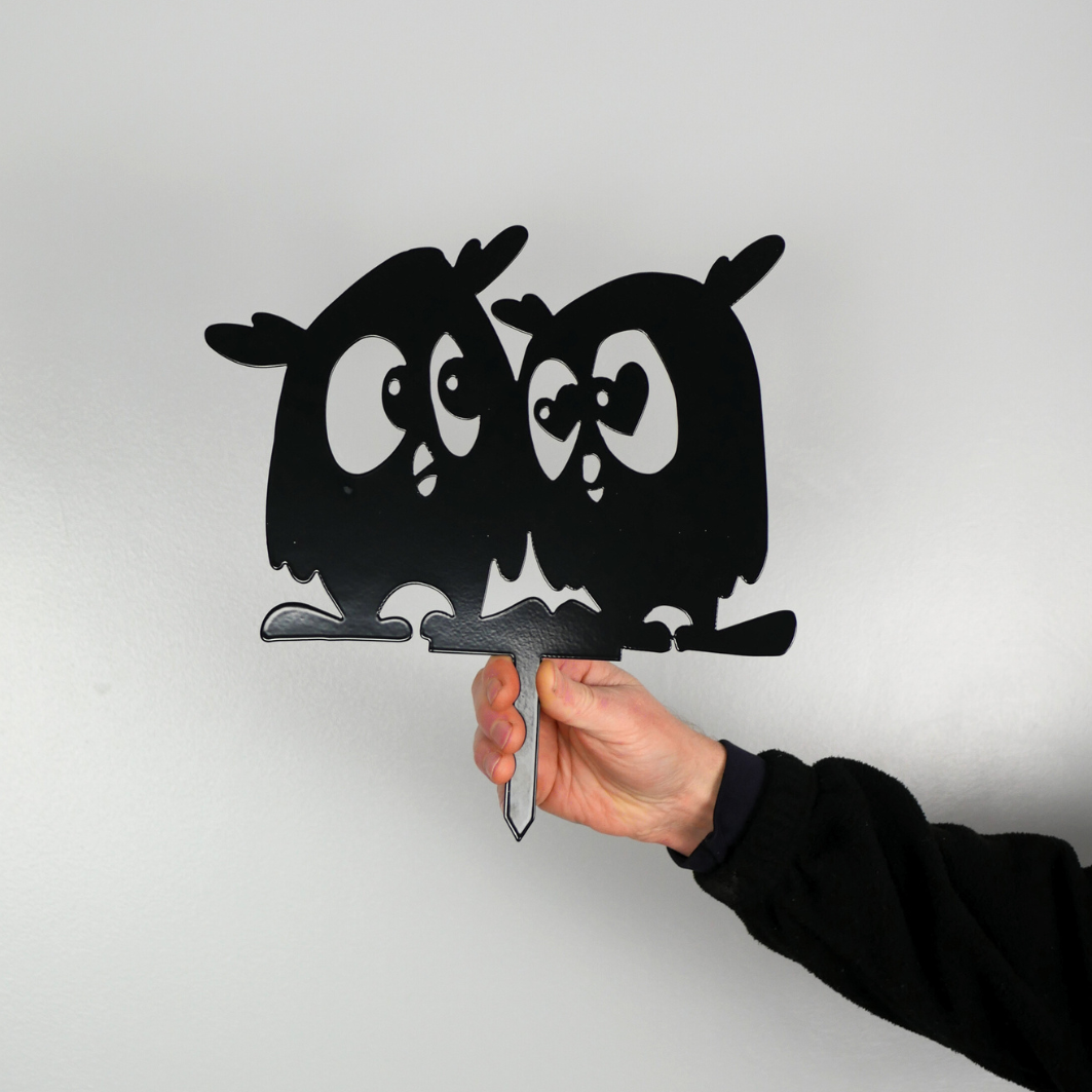 A man’s hand holding a metal black garden stake in the shape of two owls.