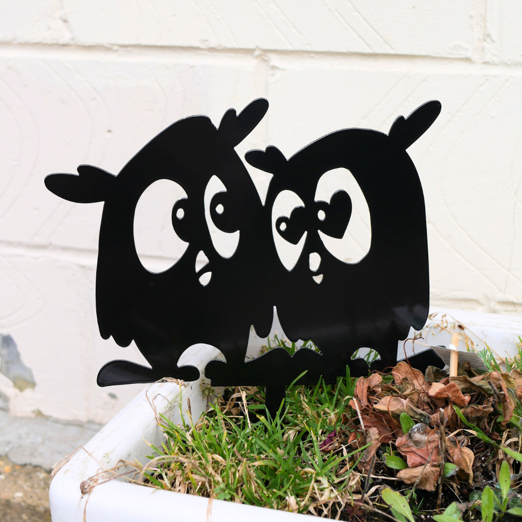 A close up of a metal black garden stake in the shape of two owls.