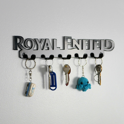 A left side view of a black metal key rack in the shape of the Royal Enfield logo, it has 5 hooks and has two sets of keys and two keyrings hanging from them.