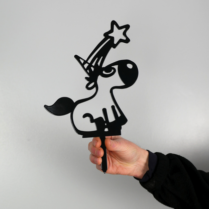 A man’s hand holding a black metal garden stake in the shape of a unicorn. It has a shooting star coming from its horn.