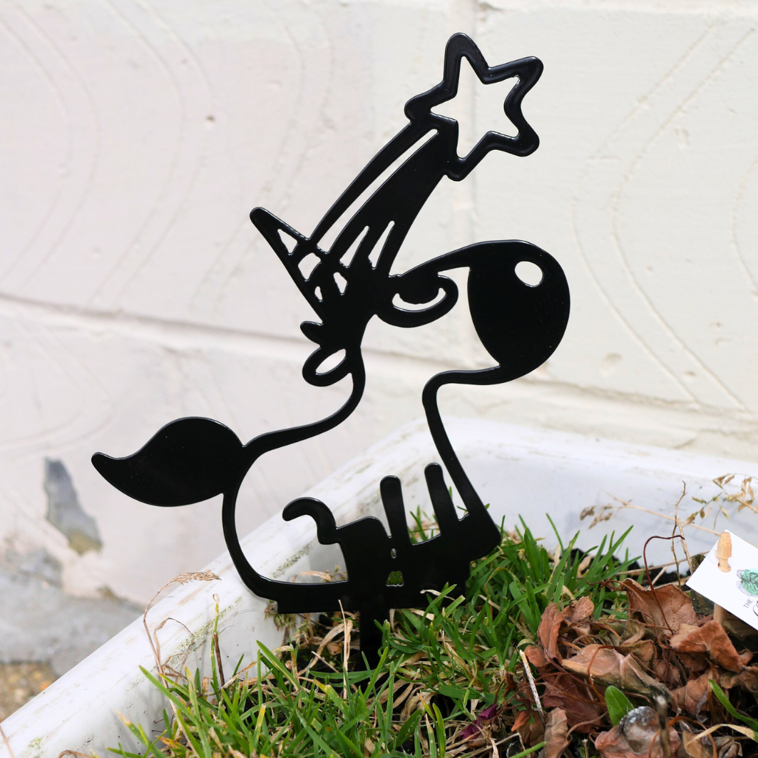A close up of a black metal garden stake in the shape of a unicorn. It has a shooting star coming from its horn.