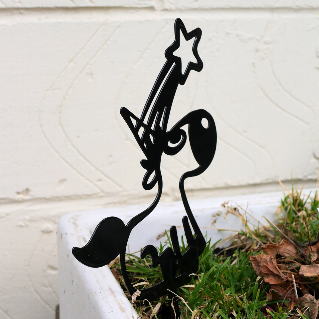 A side view of a black metal garden stake in the shape of a unicorn. It has a shooting star coming from its horn.