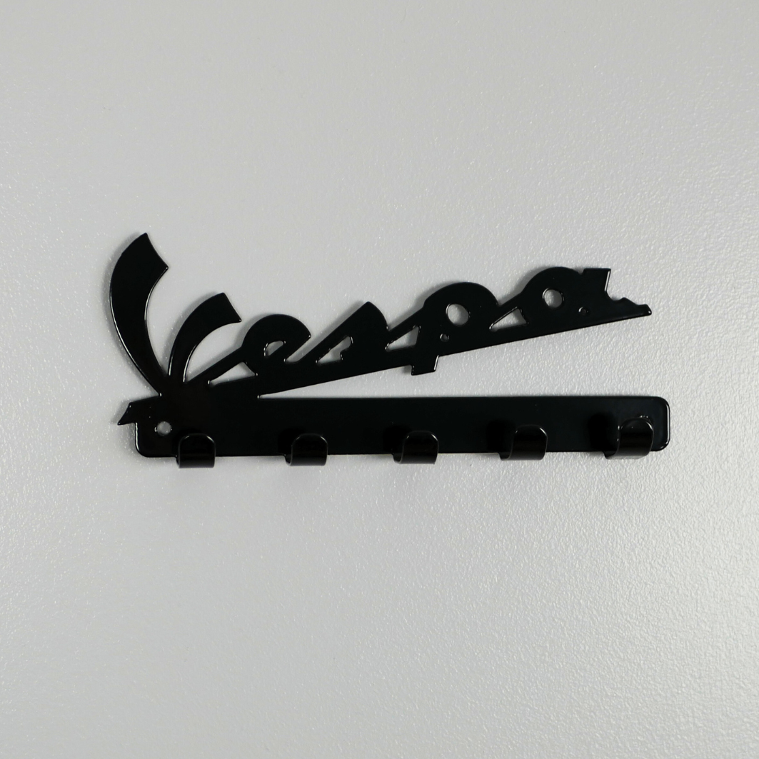A black metal key rack in the shape of the Vespa logo, it has 5 hooks.