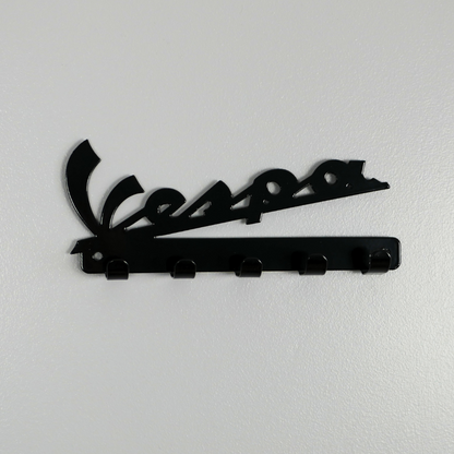 A black metal key rack in the shape of the Vespa logo, it has 5 hooks.